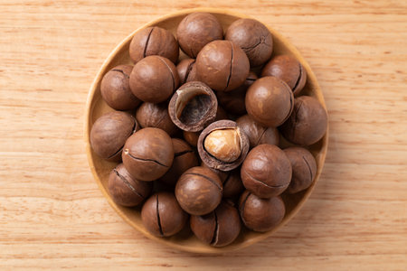 Macadamia nuts in a bowl on wooden background, Table top view