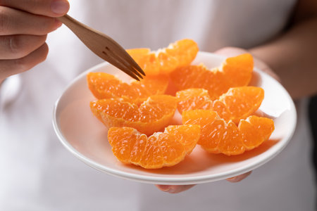 Fresh cut of Mandarin orange fruit on plate holding by hand ready to eatingの写真素材