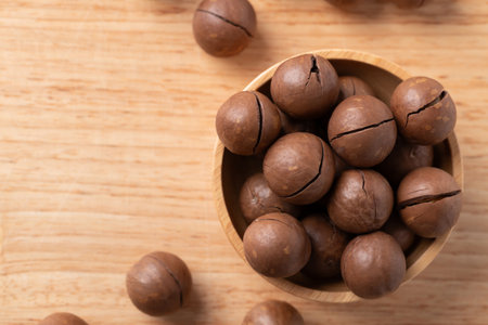 Unpeeled Macadamia nuts in bowl on wooden background, Table top viewの写真素材