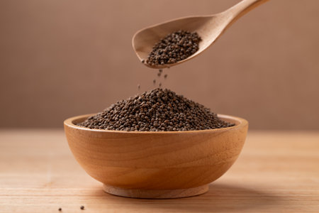Dried perilla seed in spoon pouring into a bowl on wooden backgroundの写真素材