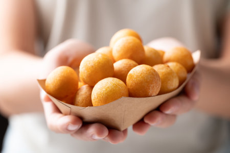 Deep fried sweet potato balls in paper bowl holding by hand, Thai street food snackの写真素材
