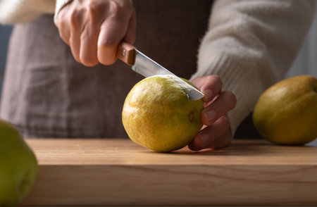 Hand holding kitchen knife and cutting pear on wooden boardの写真素材