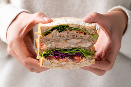 Sandwich tuna mayonnaise with whole wheat bread, lettuce, carrot, tomato and purple cabbage holding by woman handの写真素材