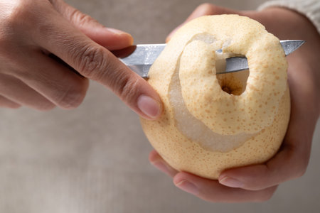 Close-up of a hand using a paring knife for peeling a fresh Asian pearの写真素材