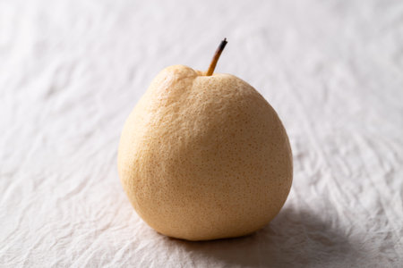 Close-up of an Asian pear on white wrinkled fabric with soft natural lightの写真素材