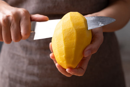 Close up of hand holding peeled mango and slicing with a knife