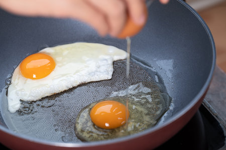Hand cracking a fresh egg into a frying pan