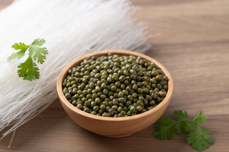 Mung beans seeds in a wooden bowl and dried glass noodles on a wooden table, raw ingredients for...
