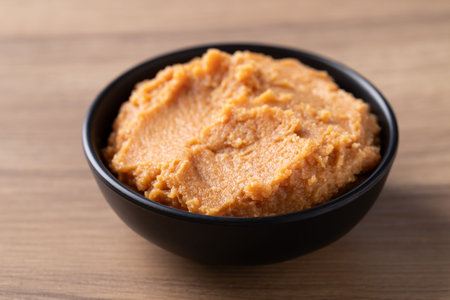 Traditional Japanese miso paste in a black bowl on a rustic wooden table. Healthy fermented soybean...