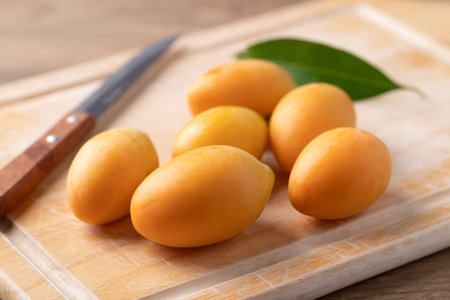 Fresh Marian plum (Mayongchid) on cutting wooden board with paring knife, Thai tropical fruit in...
