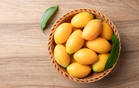 Fresh Marian plum (Mayongchid) in a wicker basket on wooden background, Thai tropical fruit in...
