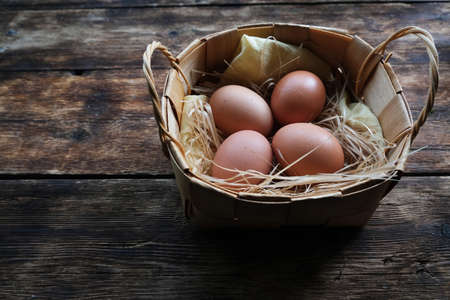 Homemade chicken egg in a wicker basket on a wooden background.の写真素材