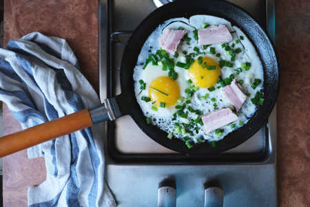 On the stove is a frying pan with rustic eggs, bacon and green onions.の写真素材