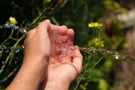 Tap water flows into the child's hands. Washes his hands in nature.