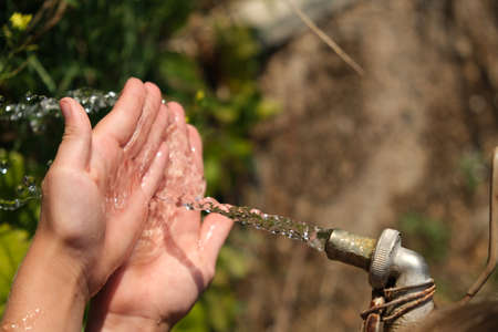 Tap water flows into the child's hands. Washes his hands in nature.