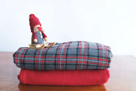 A stack of folded knitted sweaters on a wooden table and a white background, close up. Above is a...