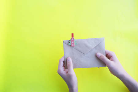In the hands of a paper envelope with a herringbone on a yellow background, close-up. Letter to...