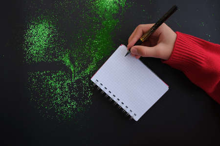 Festive green decorations, hand writes in a notebook, on a black table, flat style. Christmas...