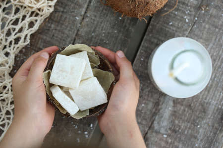 In the hands of a coconut marshmallow in a coconut scarlop. Photo on a wooden background. Natural product.の写真素材