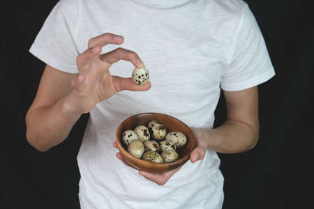 A man holds quail eggs on a dark background. Natural organic farm product. Preparing for the Easter holiday. Fresh food delivery, cardboard packaging. Raw materials for cookingの写真素材