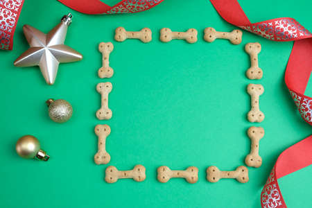 Top view of dog supplies. Frame made of dog biscuits and Christmas tree toys. Postcard with copy space. Pet shop concept isolated on green background.の写真素材