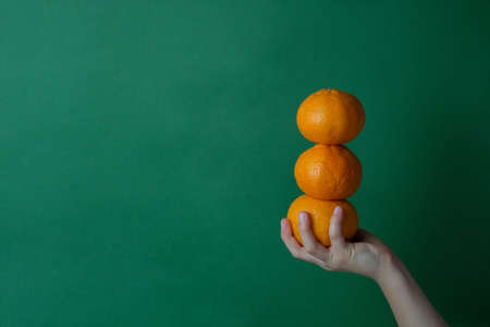 Slide tangerine in the form of a snowman in hands on a green background. Natural fresh organic...