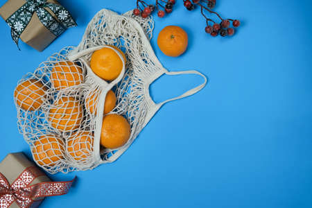 Tangerines in a string bag and New Years gifts on a blue background. Natural fresh organic fruits....
