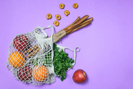 Net bag with fruits and vegetables on purple background, flat lay. Space for textの写真素材