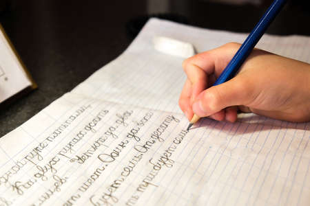 The child learns to write letters and words with a pencil in a notebook in Russian. The schoolboy...