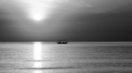 Small fishing boat is returning to shore at dawn. Black and White. Dark tone.の写真素材