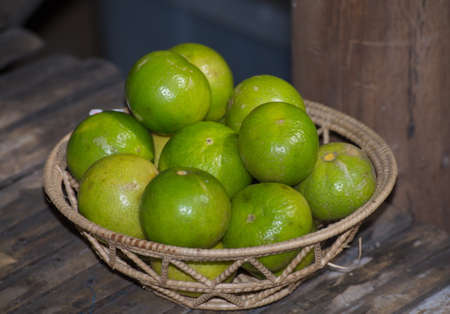 Green lemon in the wicker basket on wooden background.の写真素材