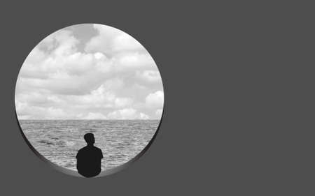 Black and White image of a man sitting on a round window sill looking at the sea.