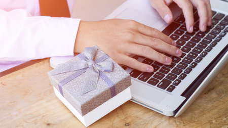 Hands of businesswoman holding a gift box and using laptop computer.の写真素材