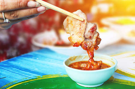 Hand hold chopsticks with pork and spicy sauce in white cup. - Image