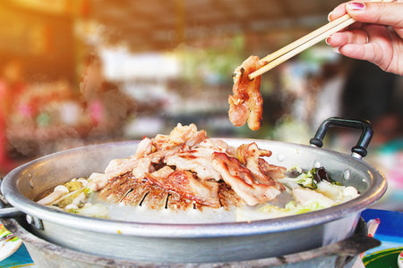 Hand hold chopsticks with Thai barbecue Grill Pork on hot pan buffet, vegetable and soup on hot pan, Moo Kra Ta (thai word) - Imageの写真素材