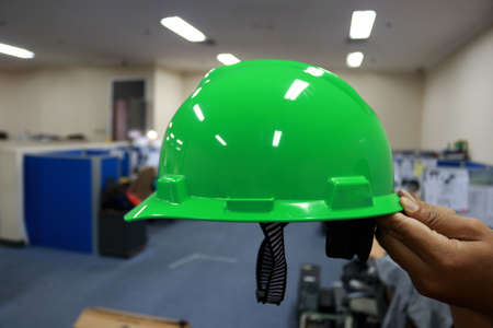 Green safety helmet in the hands of a worker in the factory.