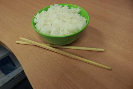 Rice in a green bowl with chopsticks on a wooden tableの写真素材