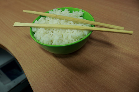 Rice in a green bowl with chopsticks on a wooden tableの写真素材