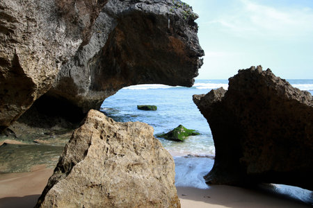 Photo of a beach scene with large rocks, sand and a cloudless blue skyの写真素材