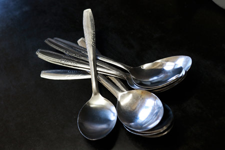A pile of spoons against a black background on a kitchen table in a house and restaurantの写真素材