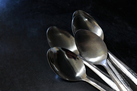 A pile of spoons against a black background on a kitchen table in a house and restaurantの写真素材