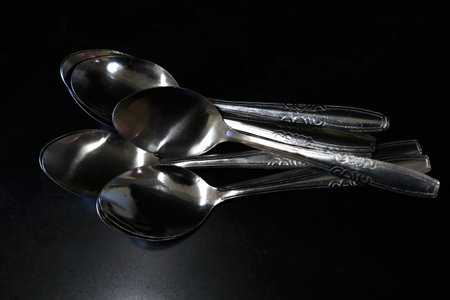 A pile of spoons against a black background on a kitchen table in a house and restaurantの写真素材