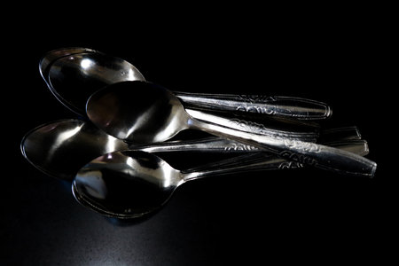 A pile of spoons against a black background on a kitchen table in a house and restaurantの写真素材