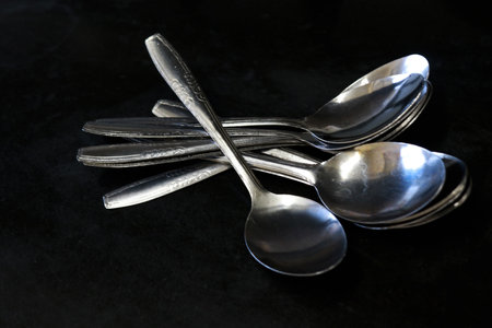 A pile of spoons against a black background on a kitchen table in a house and restaurantの写真素材