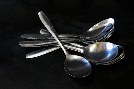 A pile of spoons against a black background on a kitchen table in a house and restaurantの写真素材