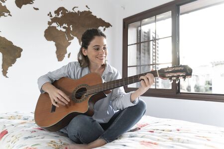 Attractive young girl plays the guitar in her room.の写真素材