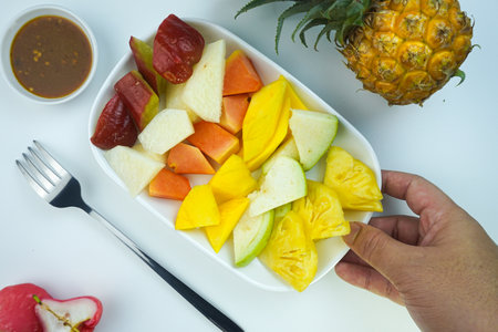 Sliced Fruit Salad, in Indonesia known as Rujak Buah or Lutis or Lotis. Served with Spicy Brown Sugar sauce and Ground Peanuts in a plate on white background with hand. Close up top view flat lay copy spaceの写真素材