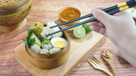 Fish cake dumplings or Siomay is a traditional food from Indonesia made of potato egg cabbage roll peanut chili lime served in a bamboo bowl on dark wood background with hand. Close upの写真素材