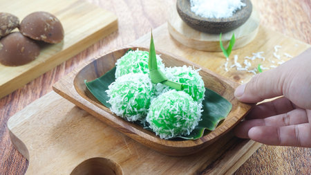 Kelepon cake or klepon is a traditional food from Indonesia made of glutinous rice flour brown sugar grated coconut served in a plate on dark wood background with hand. Close upの写真素材