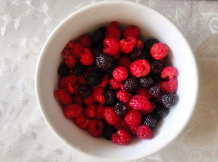 Red and black berries in a white bowl on a tablecloth